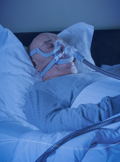 Ein im Bett schlafender Mann, der mit einem Beatmungsgerät unterstützt atmet.